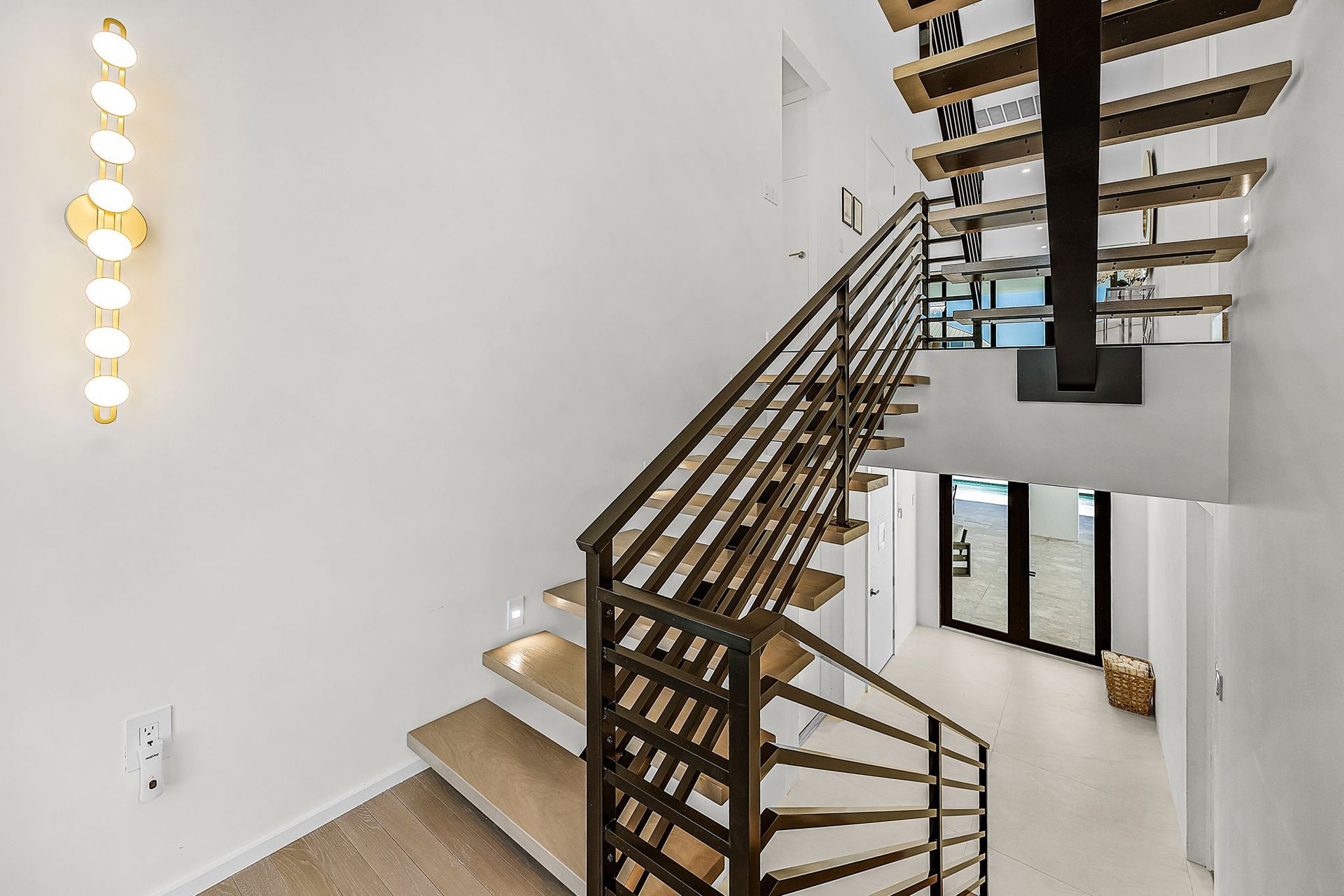 Staircase with wood steps and metal railing, leading to a lower level with glass doors. Wall sconce on the left.