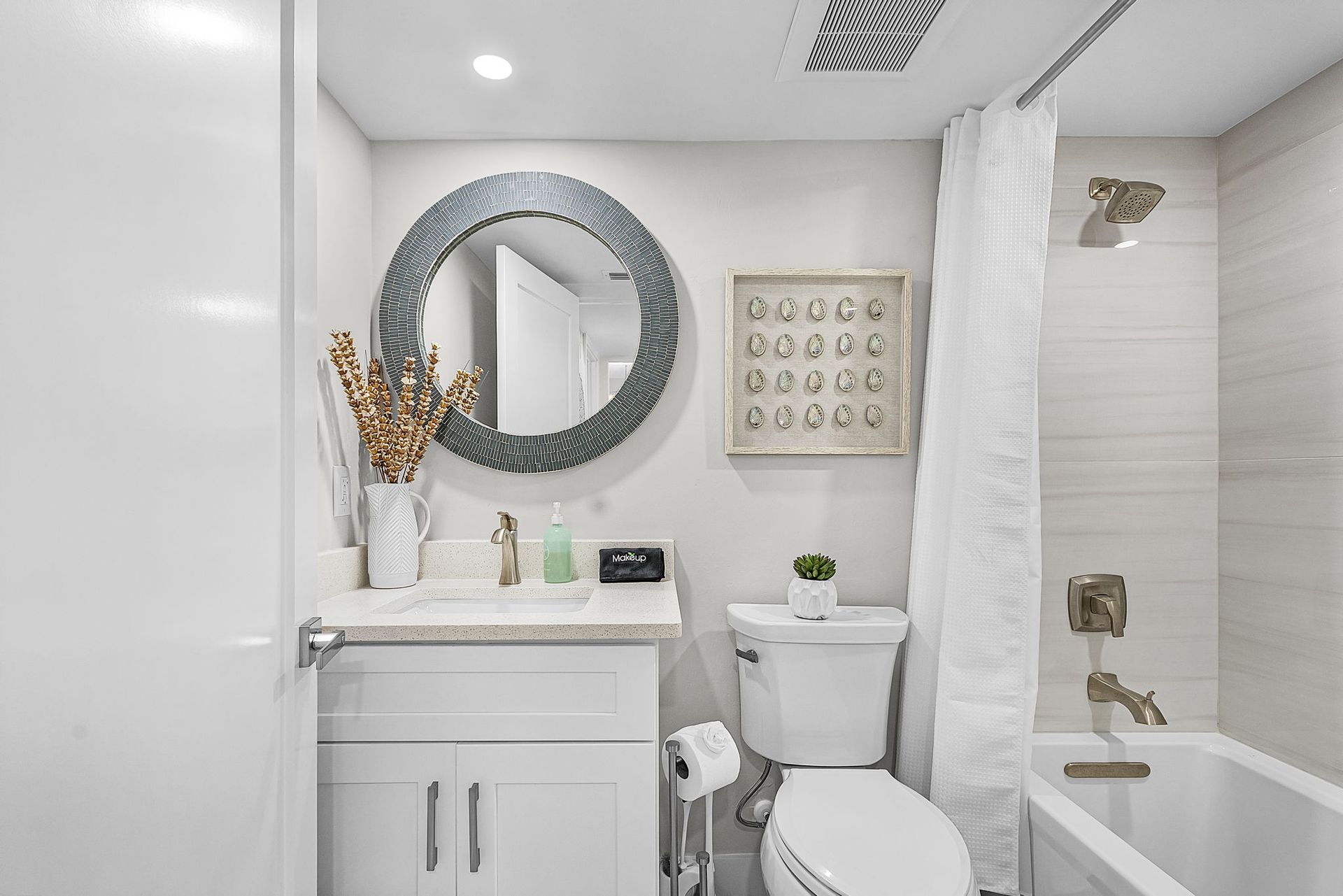 Bright, modern bathroom with white cabinetry, a round mirror, and a small bathtub.