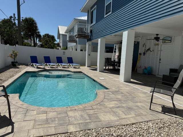 Poolside view of a house with a pool, lounge chairs, and an outdoor seating area. Blue siding and sunny day.