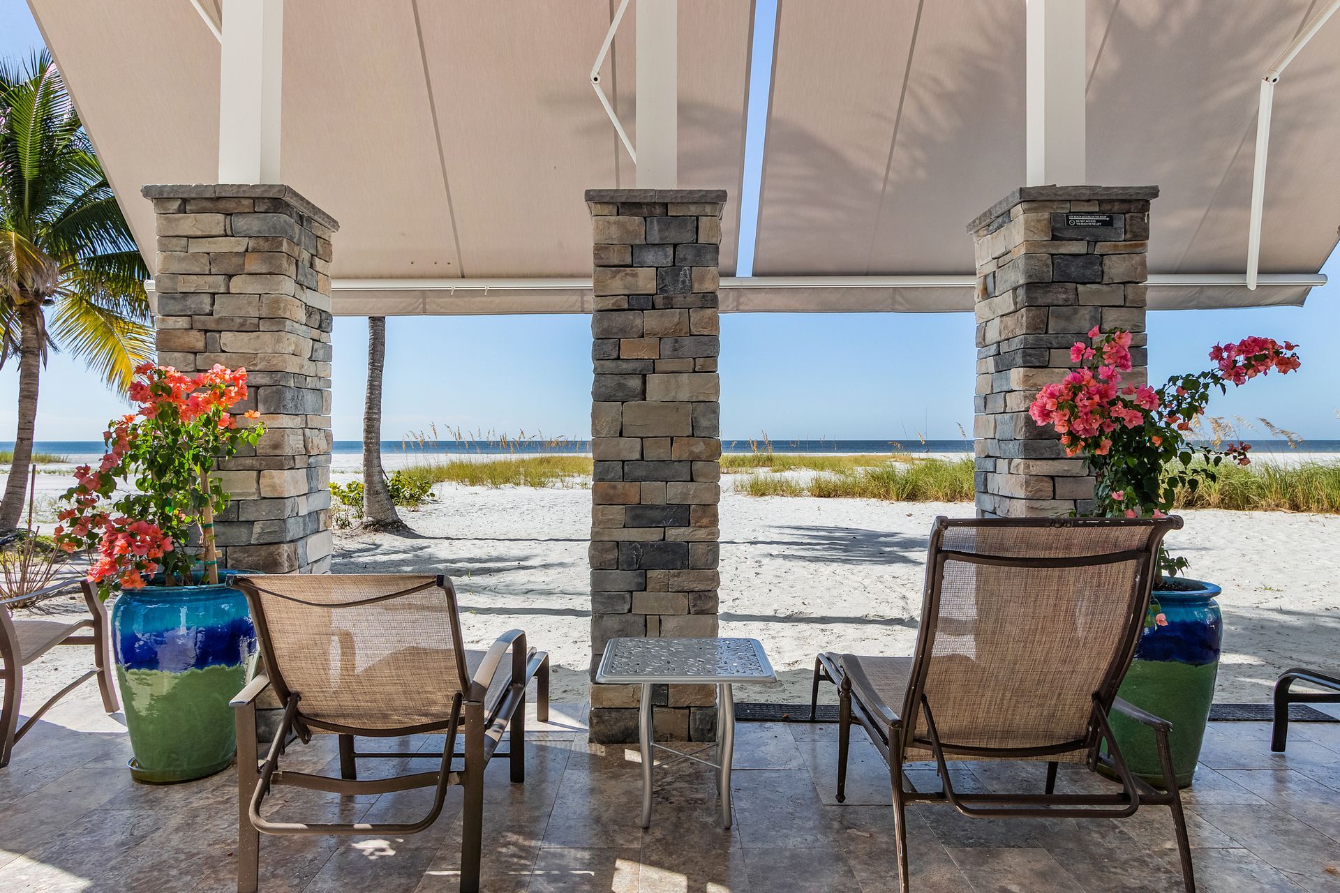 Beachfront patio with stone pillars, two chairs, potted flowers, and ocean view