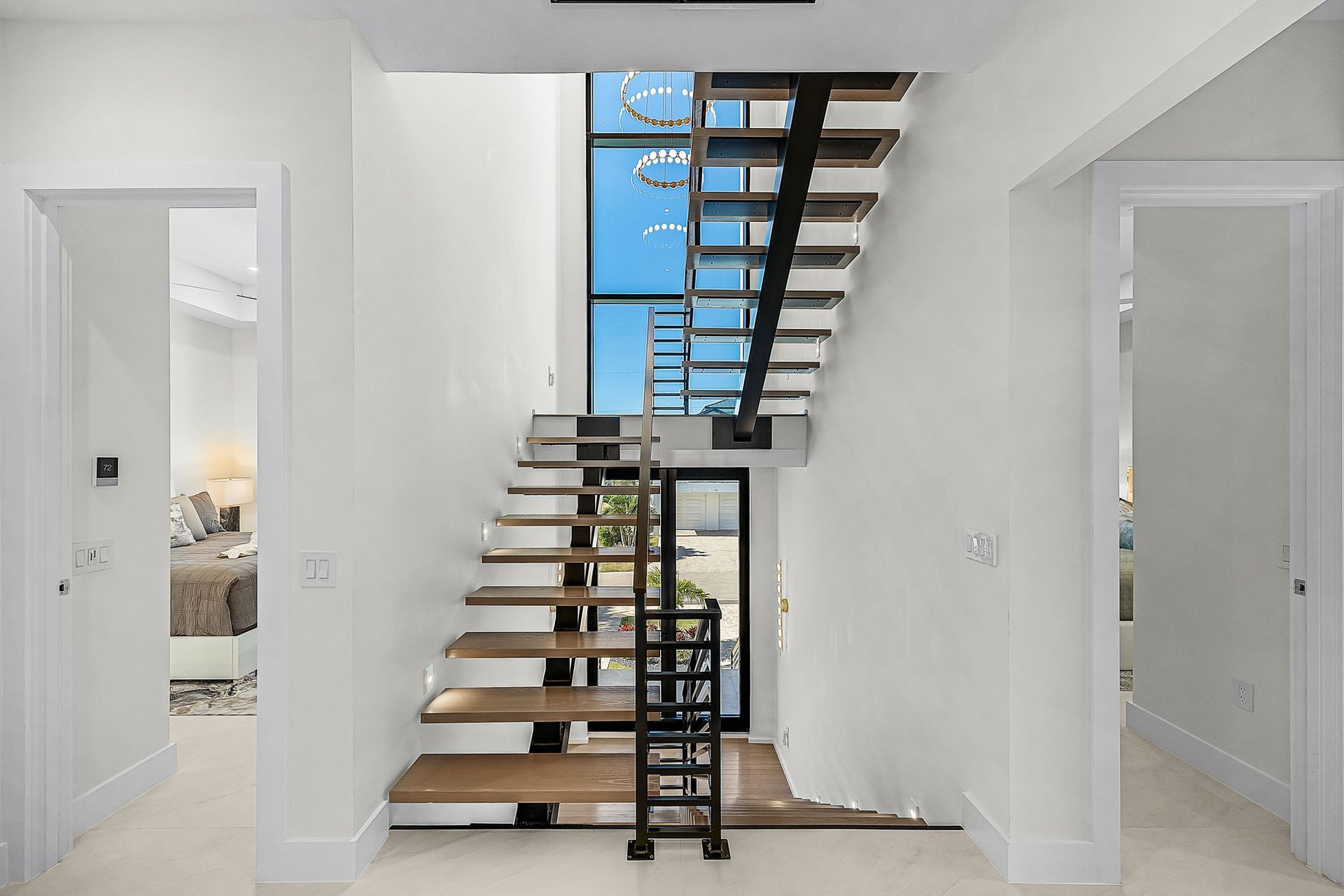 Hallway with floating stairs, high ceiling, natural light, and open doorways.