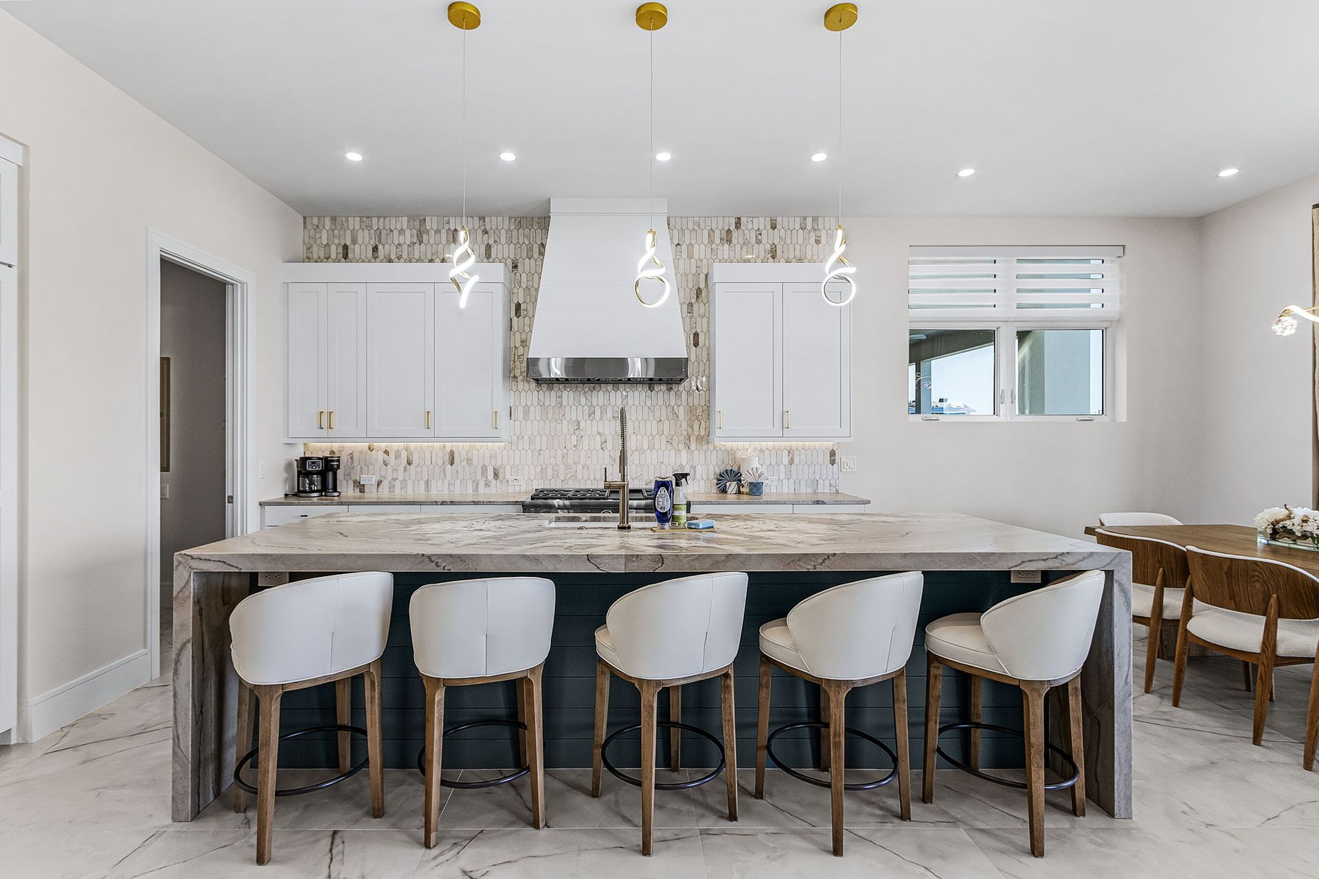 Modern kitchen with white cabinets, island with stools, and decorative light fixtures.