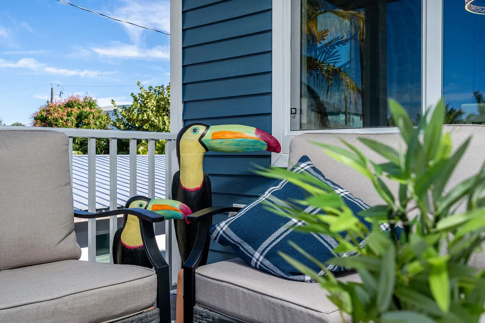 Outdoor seating area with blue siding, toucan statues, and a patterned pillow.
