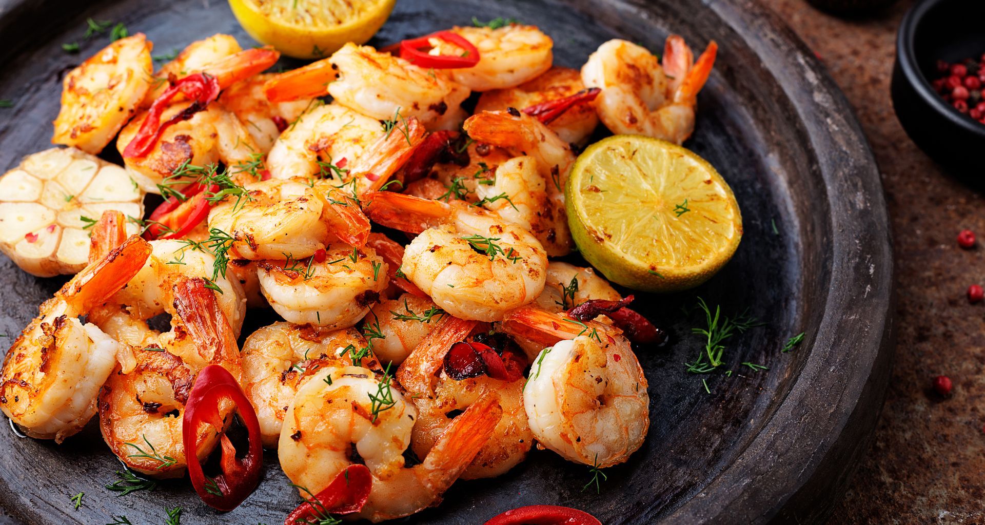 Sautéed shrimp with lemon, chili peppers, garlic, and herbs on a dark plate.