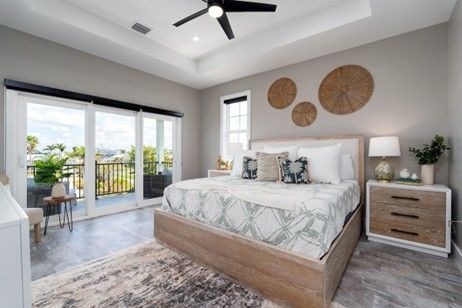 Bedroom with wooden bed, light gray walls, sliding door to balcony, decorative wall hangings.