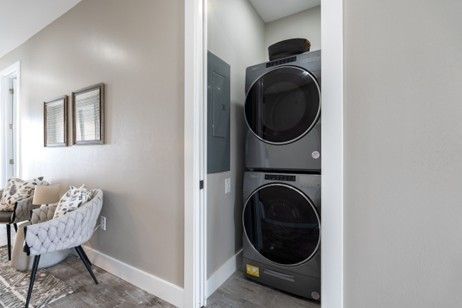 Stacked gray washer and dryer in a narrow closet; hallway with art and chair.