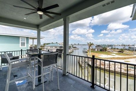 Balcony with outdoor seating overlooking a canal and coastal homes under a sunny sky.