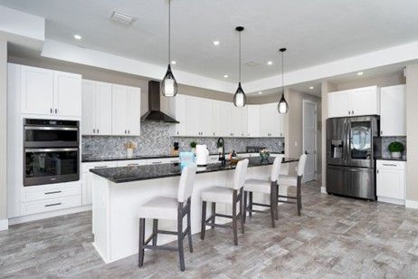 Modern kitchen with white cabinets, island with stools, and dark appliances.