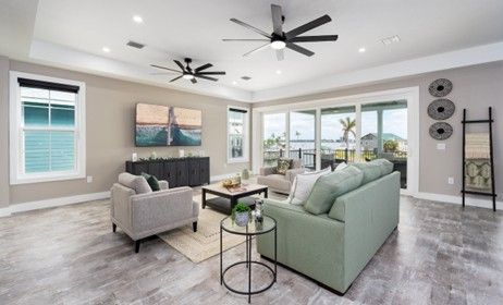 Spacious living room with gray flooring, light green sofa, and black ceiling fans.