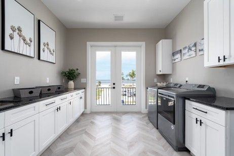 Laundry room with white cabinets, dark countertops, and gray appliances, facing double doors with a water view.