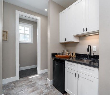 Small kitchen area with white cabinets, a black countertop, and a small refrigerator.