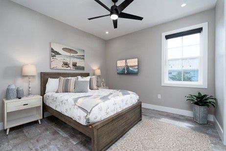 Bedroom with a wooden bed, nightstand, and beach-themed artwork; gray walls and flooring.