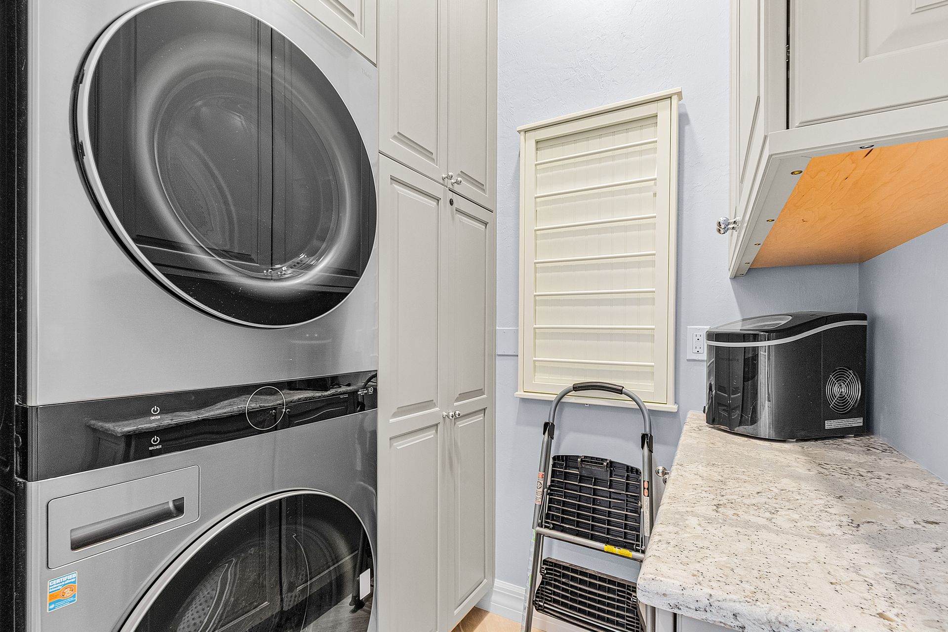 Laundry room with stacked washer and dryer, white cabinets, and a countertop coffee maker.