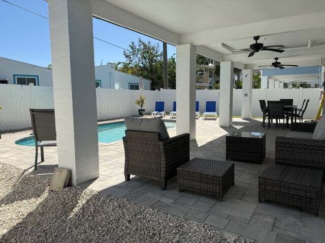 Covered outdoor seating area with pool. Wicker furniture, white pillars, ceiling fans, and a dining table.
