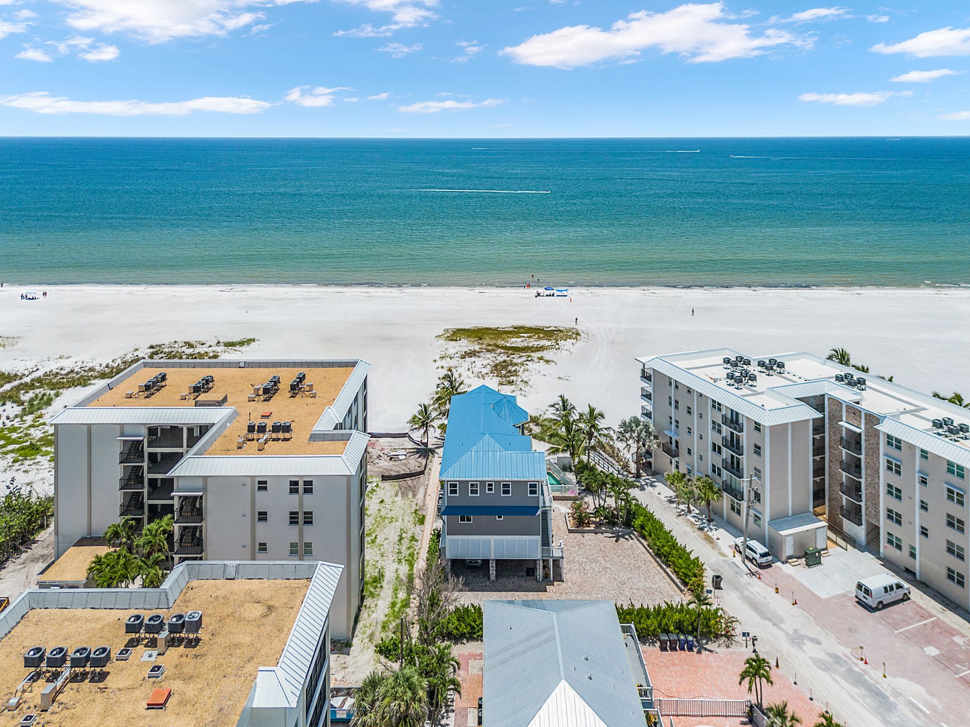 Aerial view of beachside condos with a blue-roofed building and turquoise ocean beyond.