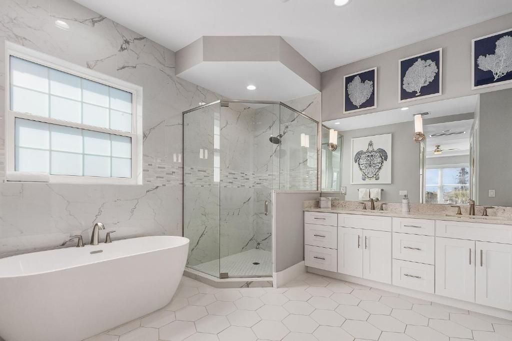 Spacious white bathroom with freestanding tub, glass shower, double vanity, and hexagon tile floor.