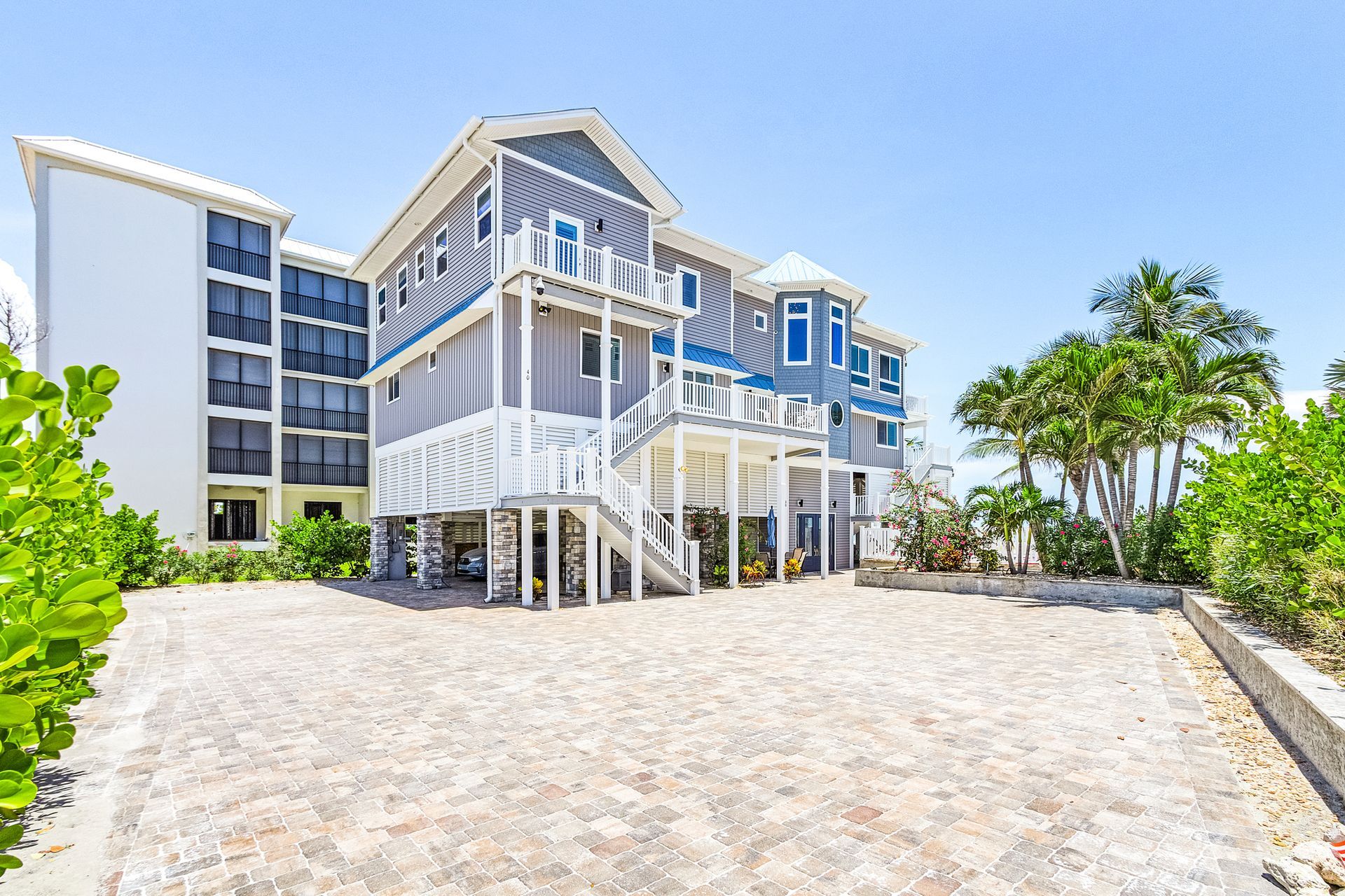 Modern beachfront house with white stilts and balconies on a sandy lot under a clear blue sky