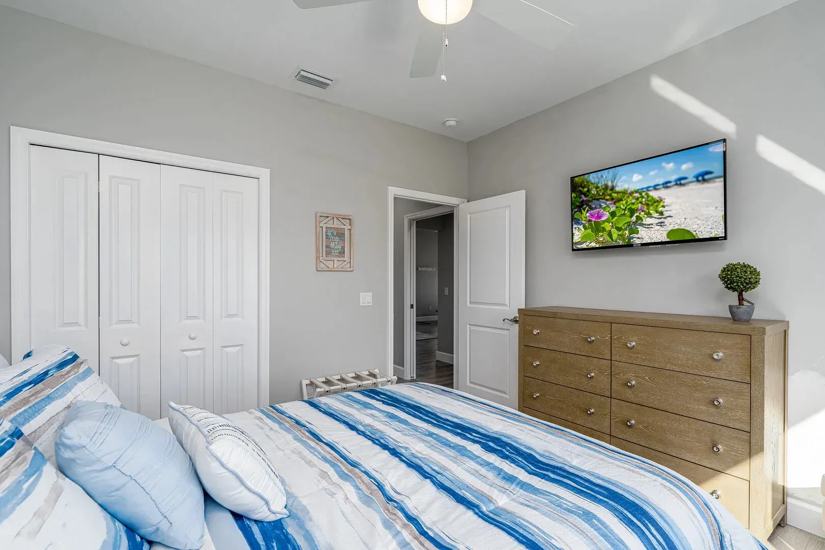 Bedroom with blue and white striped bedding, closet, dresser, TV, and open doorway to a bathroom.