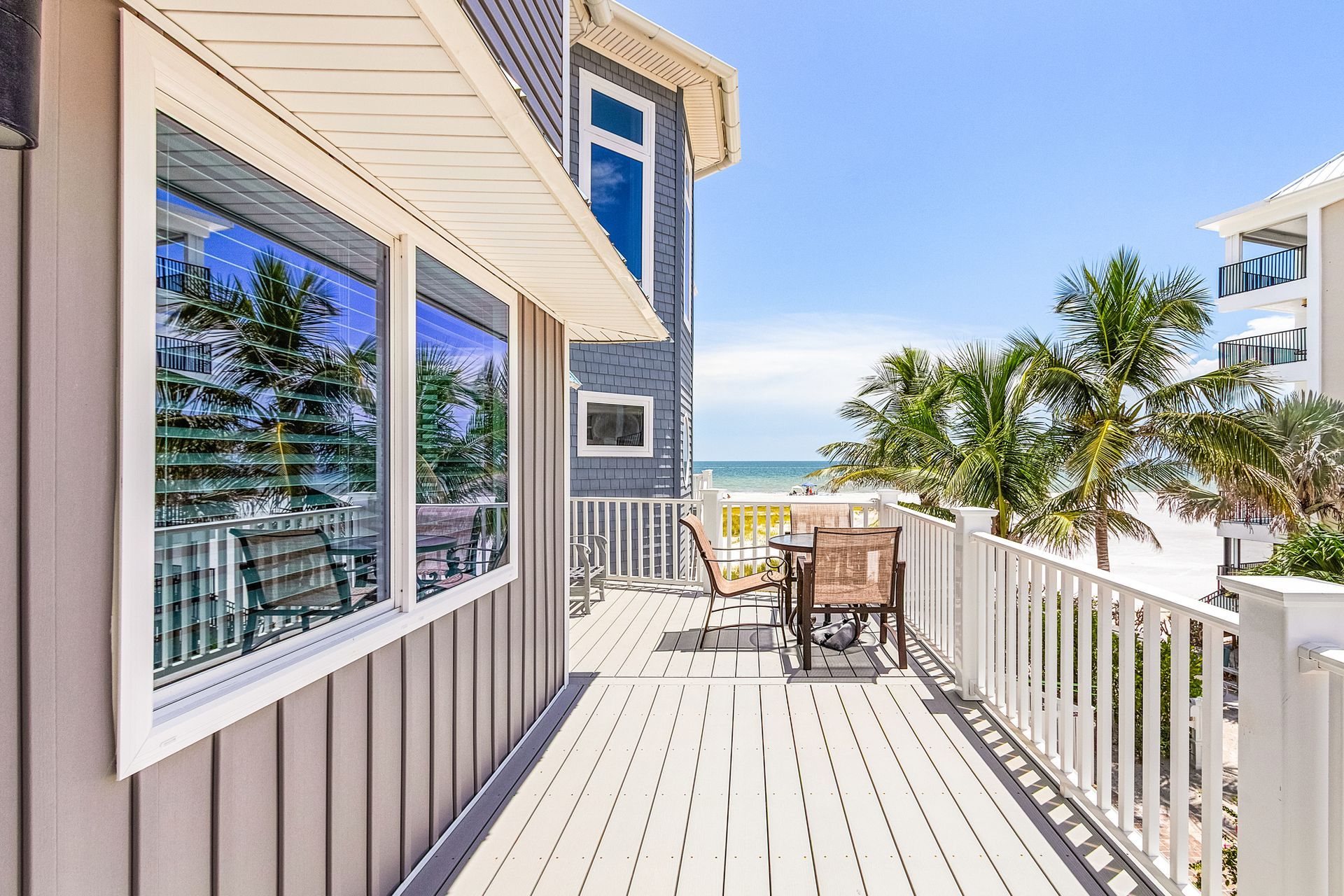 Sunny seaside deck with white railing, outdoor table, and ocean view