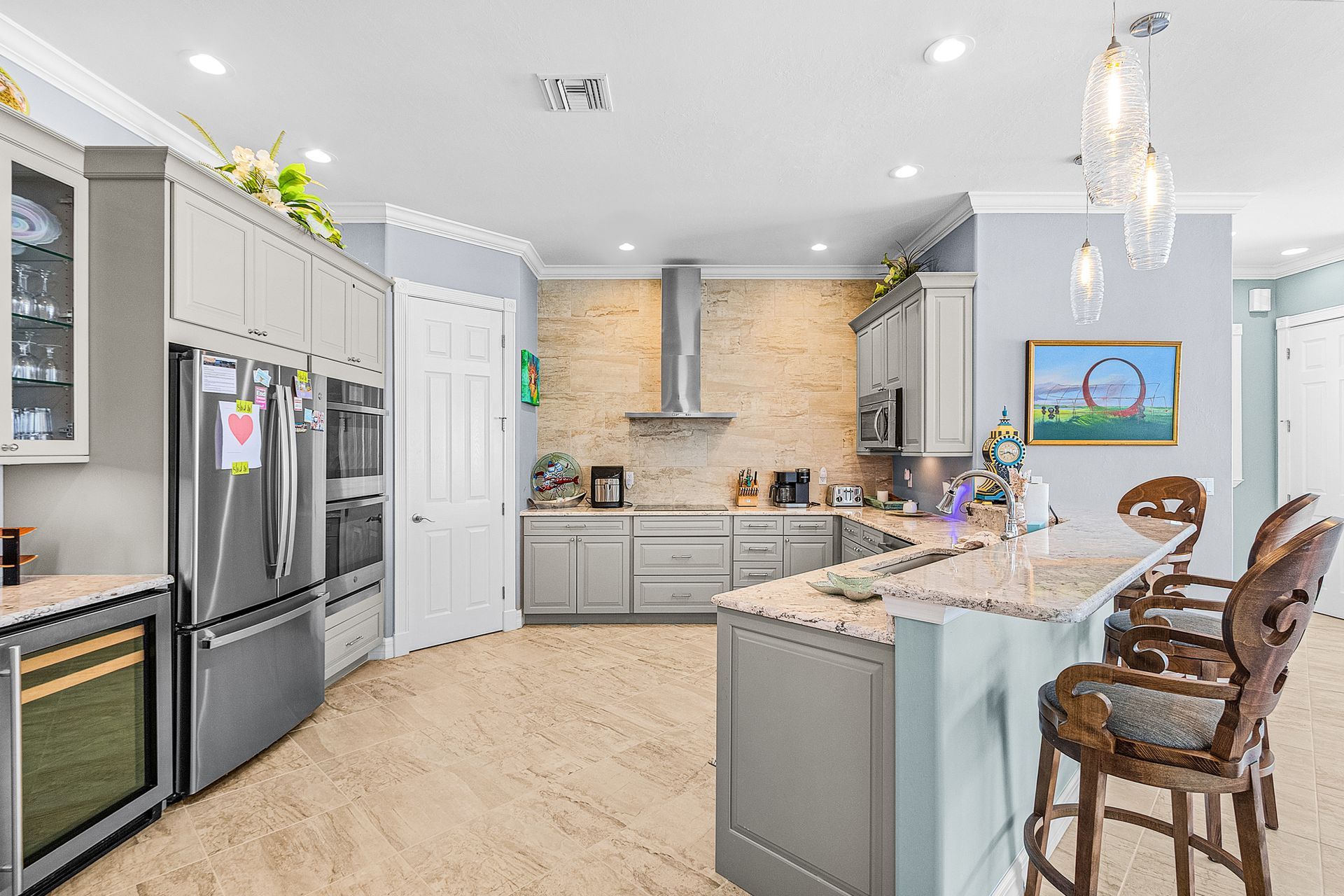 Bright modern kitchen with gray cabinets, stainless fridge, island seating, and stainless range hood