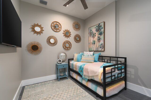 Bedroom with gray walls, decorative mirrors, daybed with teal, pink, and white bedding, art, and rug.