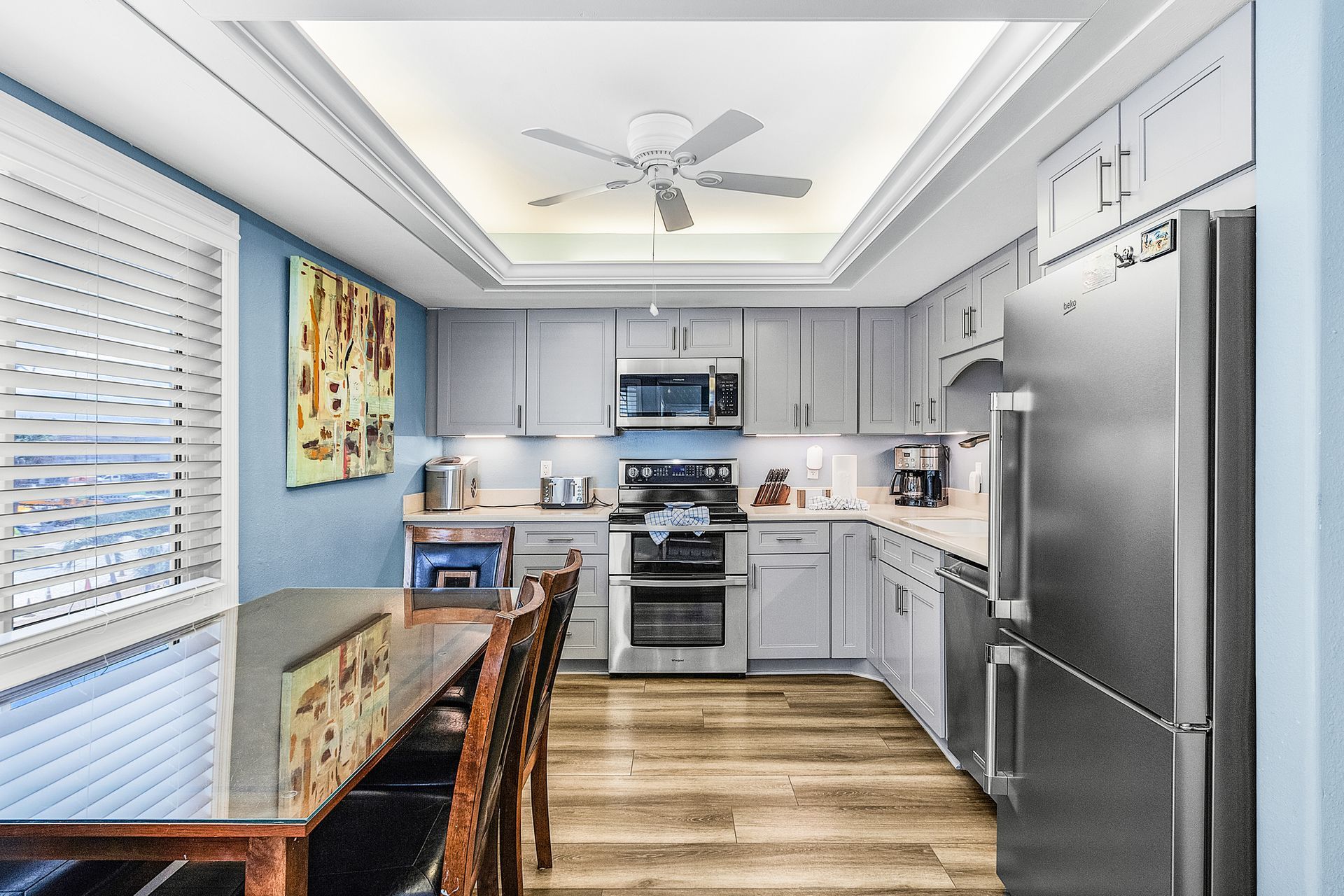 Modern kitchen with stainless steel appliances, gray cabinets, wood floor, and a dining table by the window