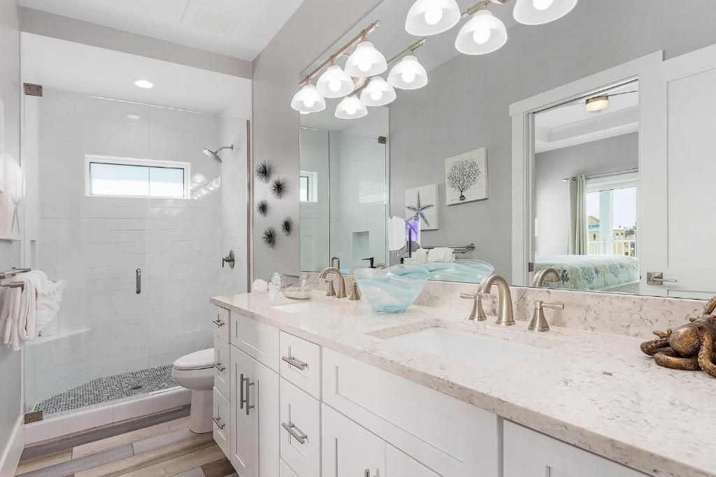 White bathroom with a double vanity, a glass-walled shower, and gray walls.