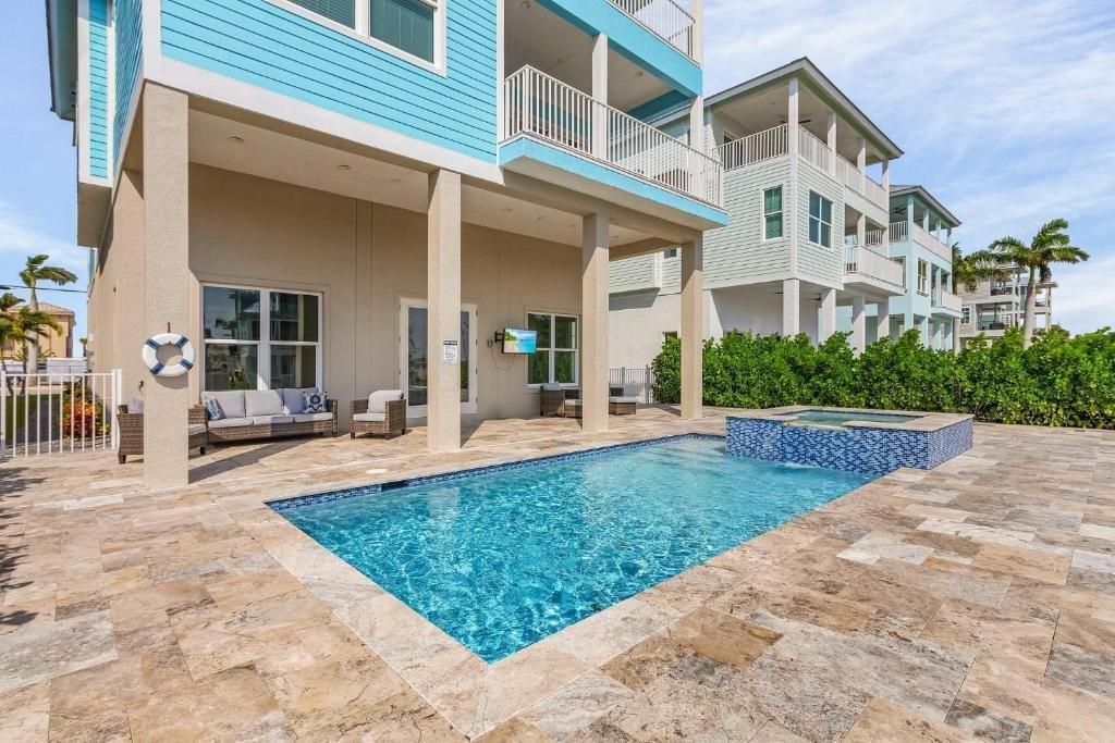 Swimming pool outside a light blue and white house, sunny day.