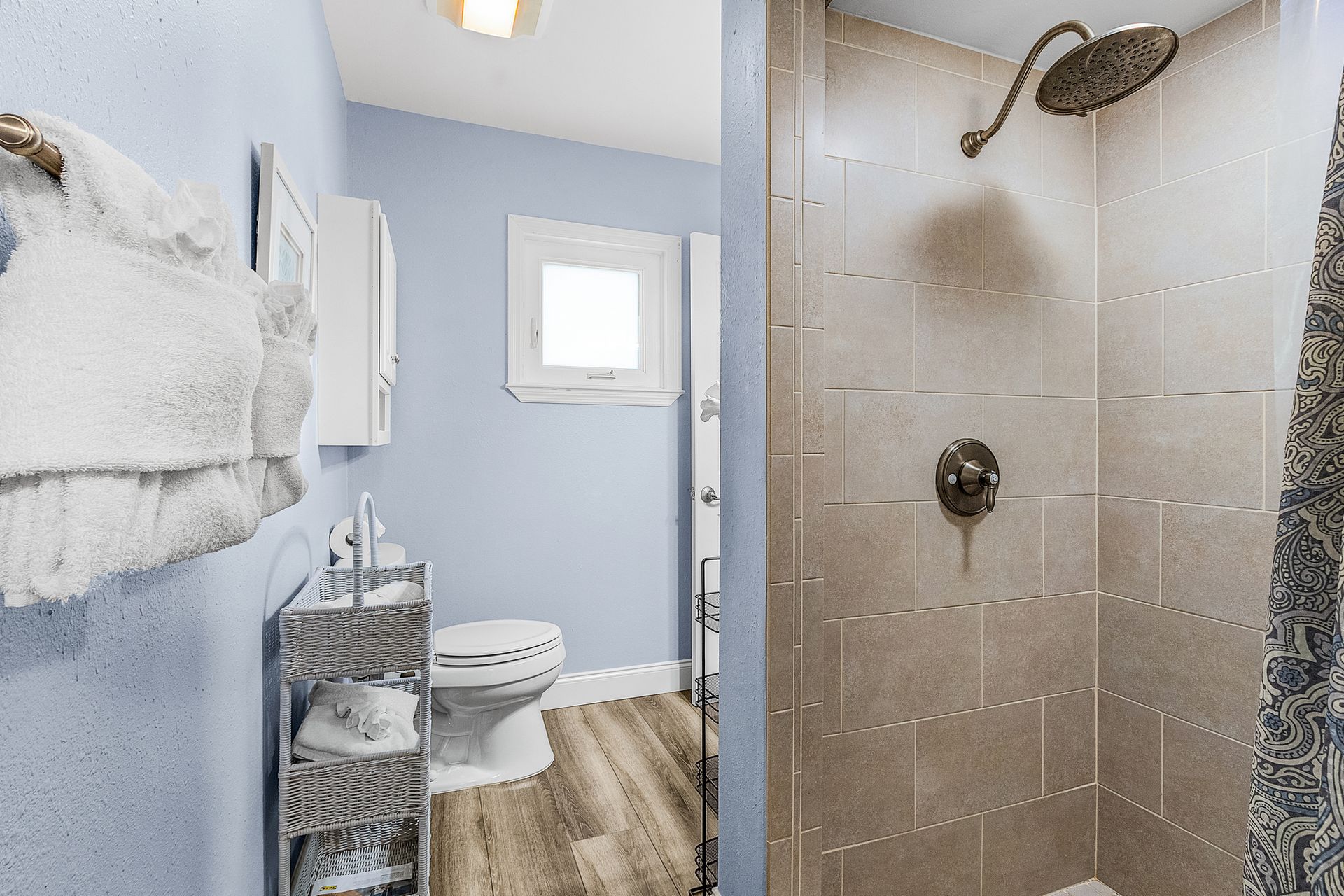 Small bathroom with shower, toilet, blue walls, white towels, and wood-look floor.
