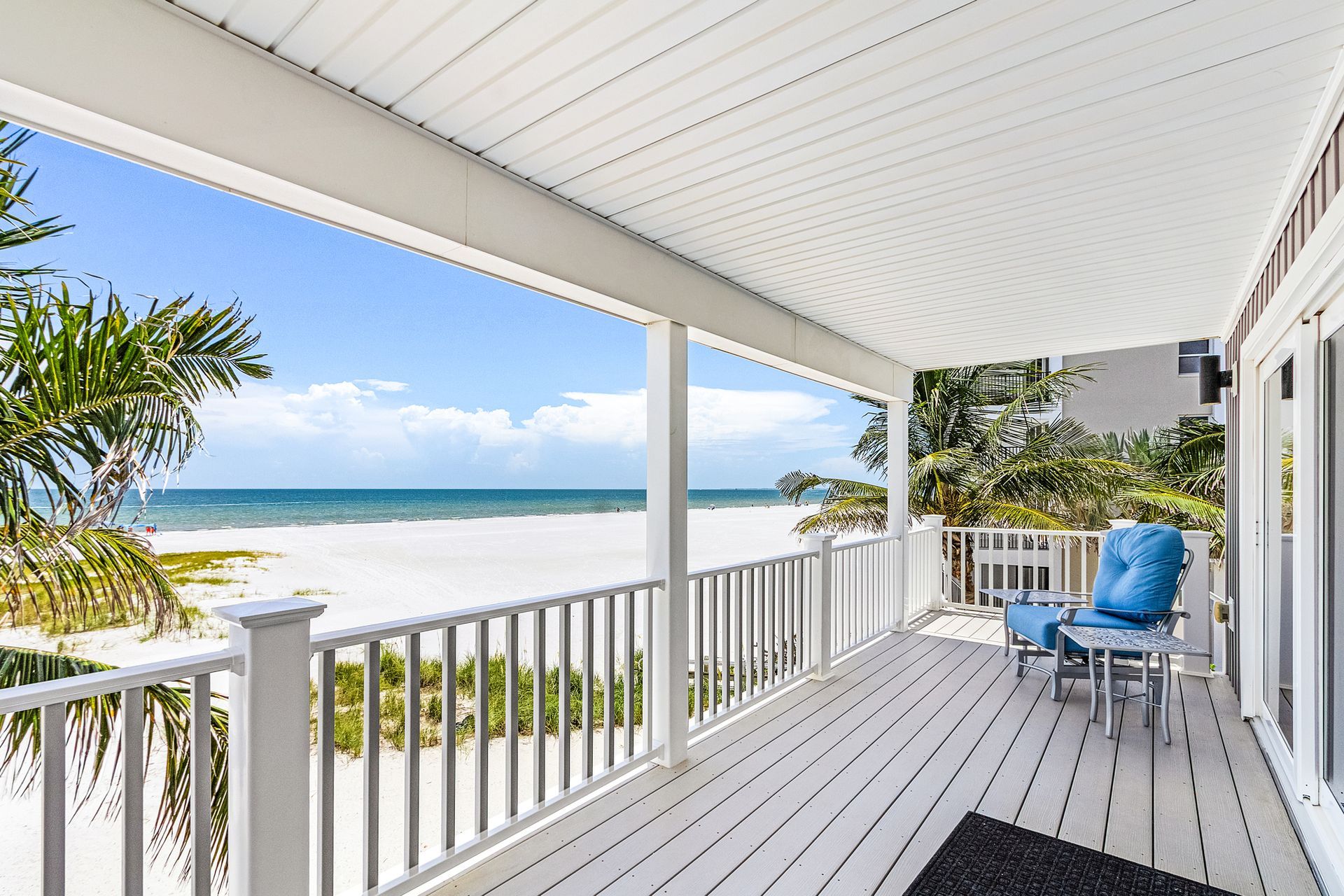 Beachfront porch with white railings, blue chair, and ocean view under a bright sky