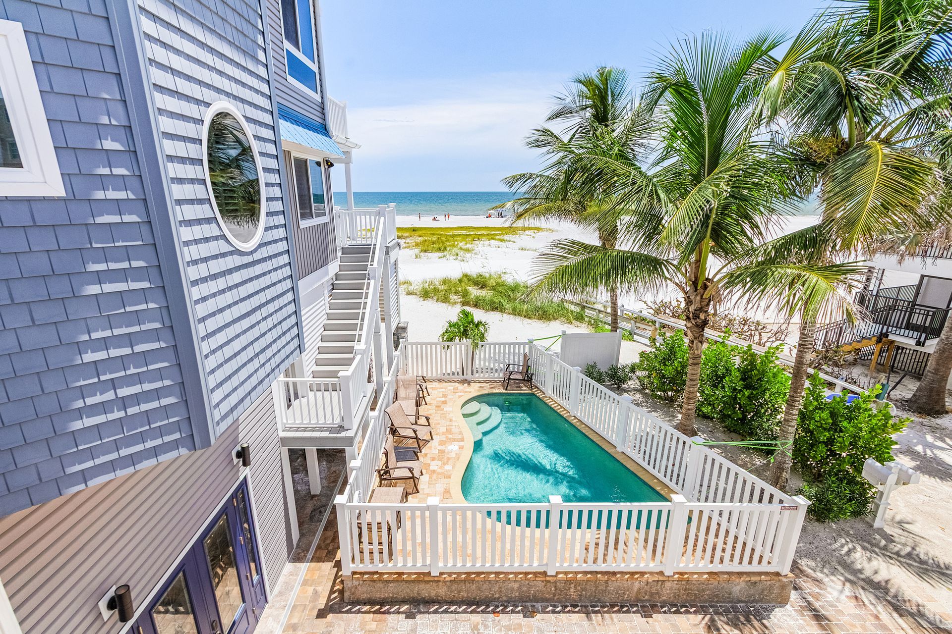 Beachfront house with a turquoise pool, white fence, palm trees, and ocean view