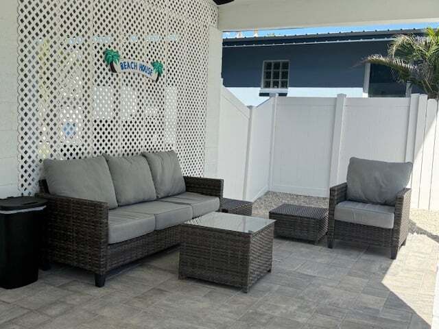 Patio with gray wicker furniture: sofa, armchair, and coffee table. White lattice backdrop with