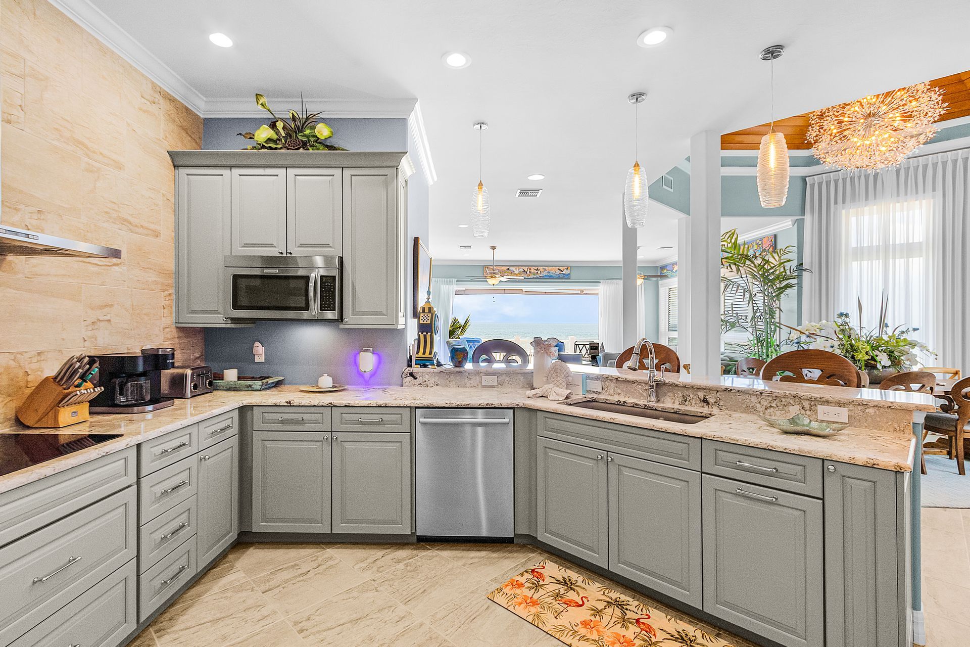 Bright kitchen with gray cabinets, granite island, stainless appliances, and chandelier lighting.