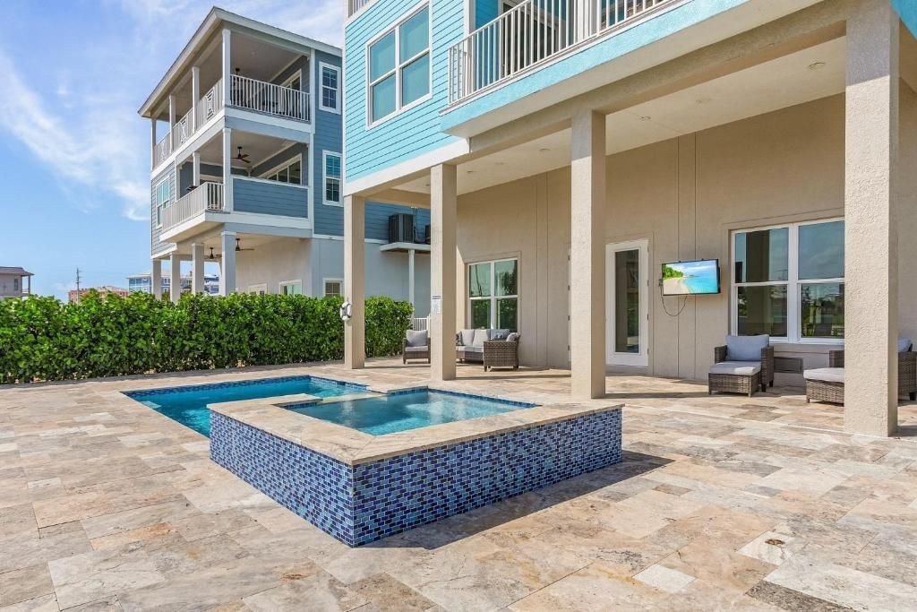 Outdoor patio with pool, spa, and seating under a blue and beige coastal home.