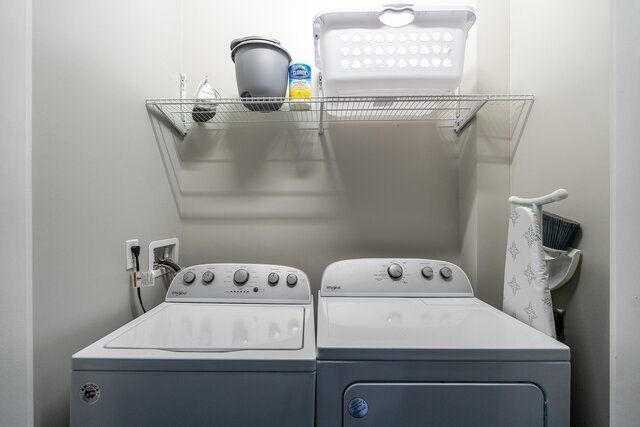 Laundry room with washer, dryer, shelf with laundry basket, cleaning supplies, and ironing board.