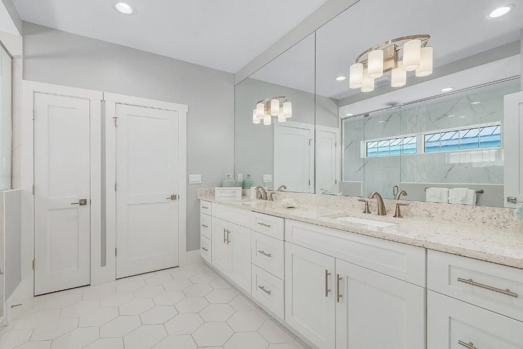 White bathroom with double vanity, large mirror, hexagon tile floor, and white cabinetry.