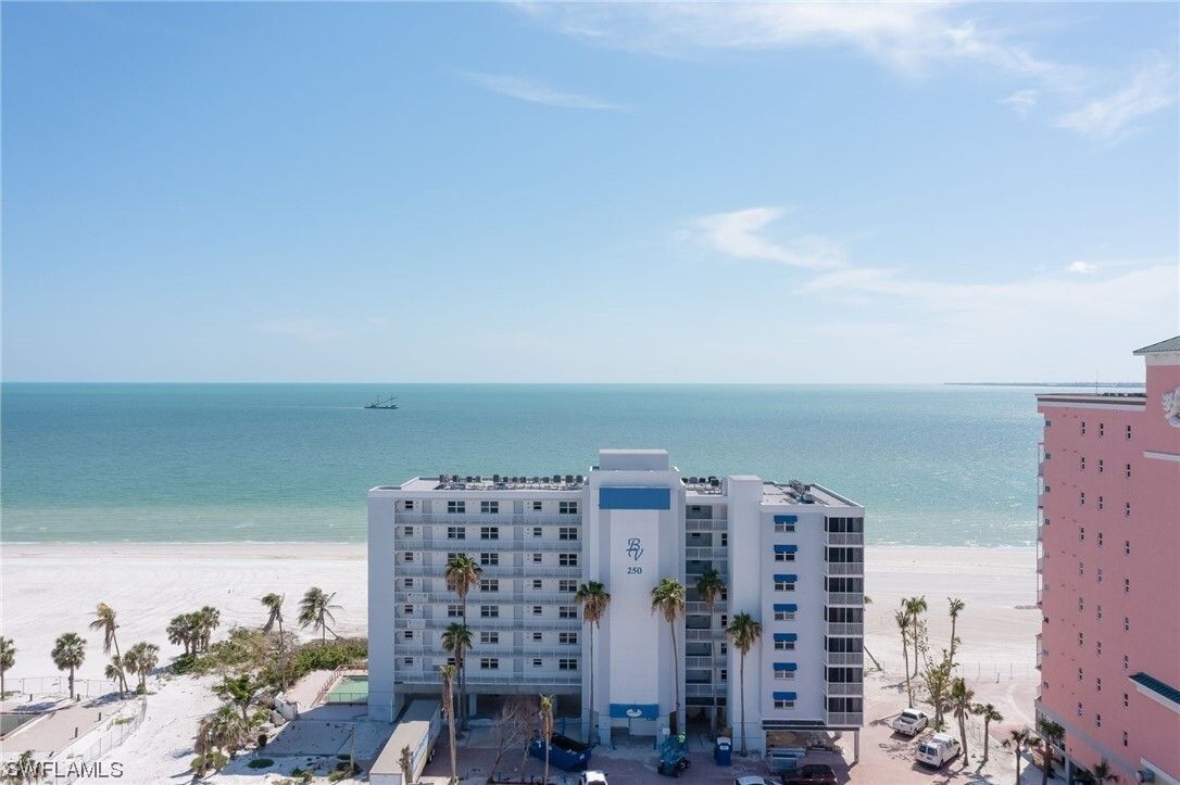 Beachfront condominium building on a sandy beach under a blue sky.