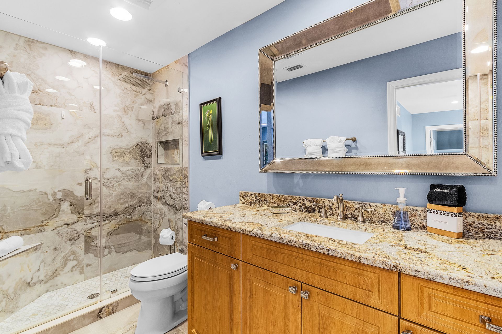 Modern bathroom with stone shower, wooden vanity, large mirror, and granite countertop