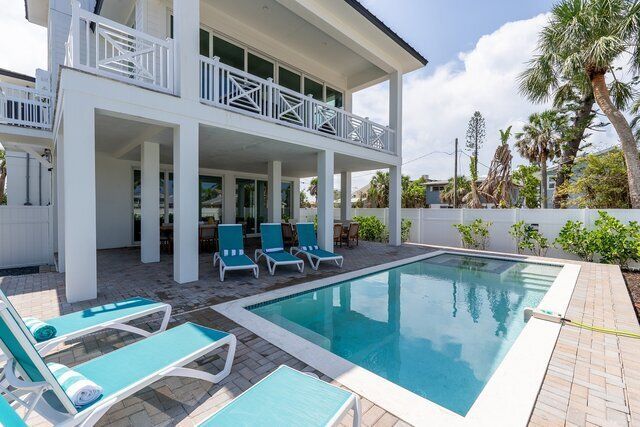 White beach house with pool, lounge chairs, and palm trees.