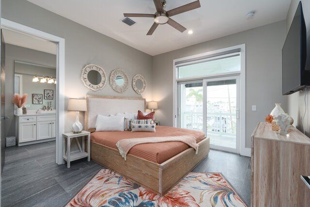 Bedroom with bed, mirrors, and door to a balcony. Grey walls, wood floors, orange bedding, and colorful rug.