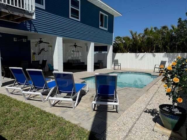 Blue house with pool and lounge chairs. Sunny outdoor setting with flowers.