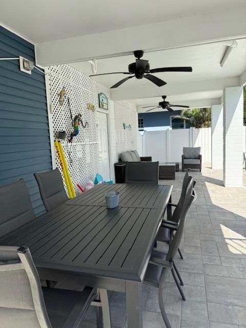 Outdoor patio with dining table and seating, under a covered area with ceiling fans.