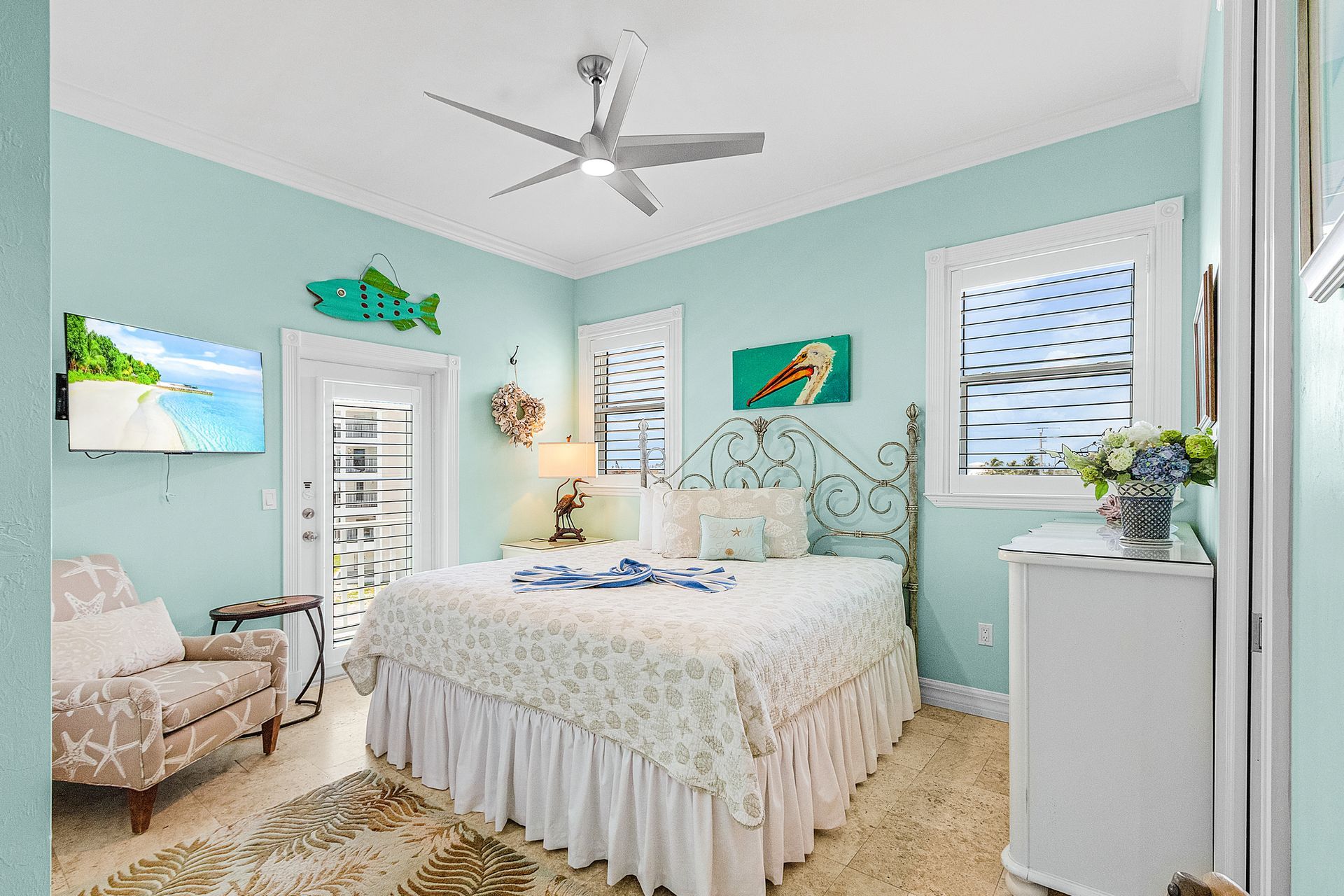 Bright aqua bedroom with white bed, fish decor, wicker chair, and sunlit windows