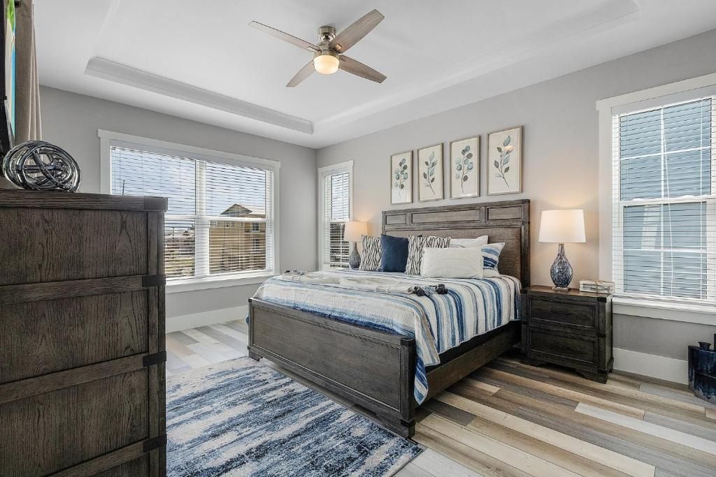 Bedroom with a gray-blue color scheme; bed with decorative pillows, wooden furniture, and framed art.