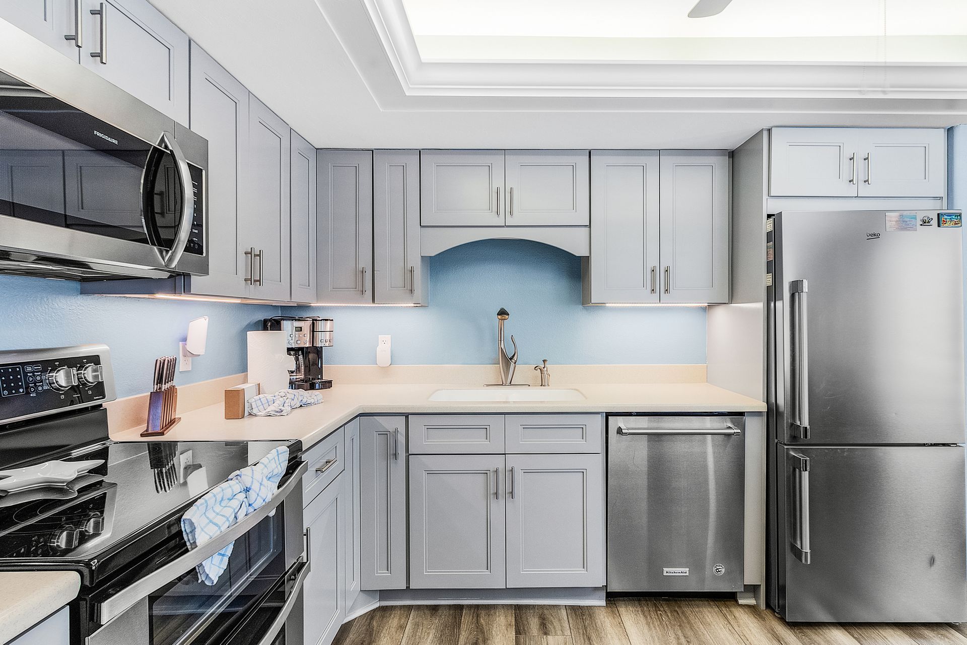 Modern gray kitchen with stainless steel appliances, white countertops, and wood flooring