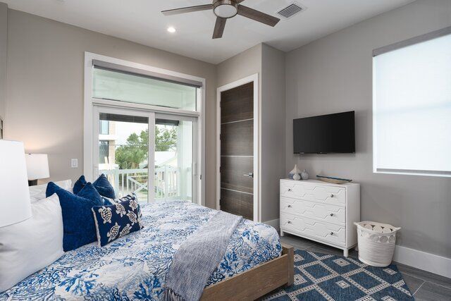 Bedroom with bed, blue patterned bedding, balcony access, TV on wall, and white dresser.