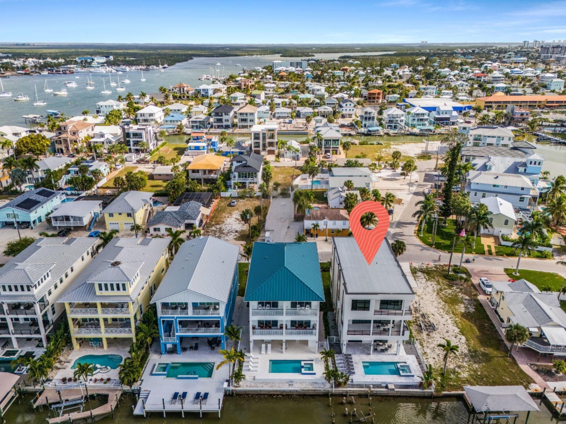 Aerial view of waterfront houses with pools. A pin indicates the middle house.
