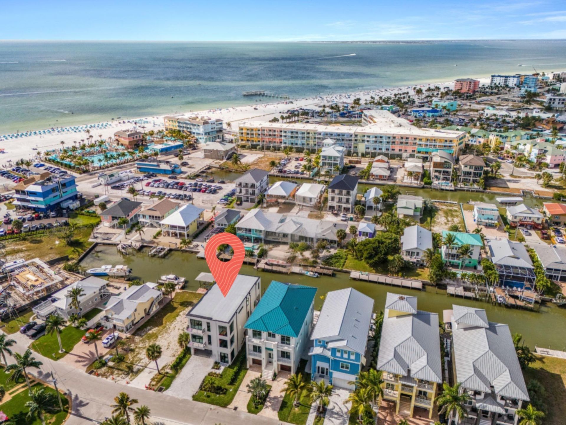 Aerial view of beachside houses, some with boats in canal, blue ocean and beach in background.