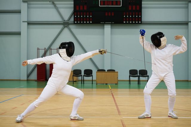 Two Fencers on a Court With a Scoreboard in the Background