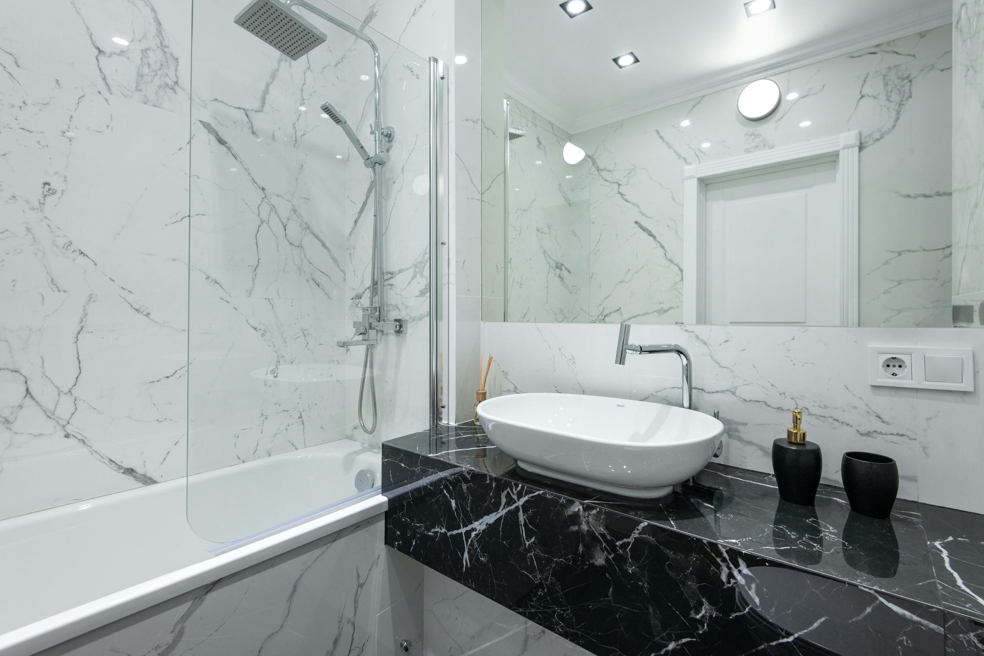 white tiled bathroom with shower in tub and sink on top of a black marbled countertop